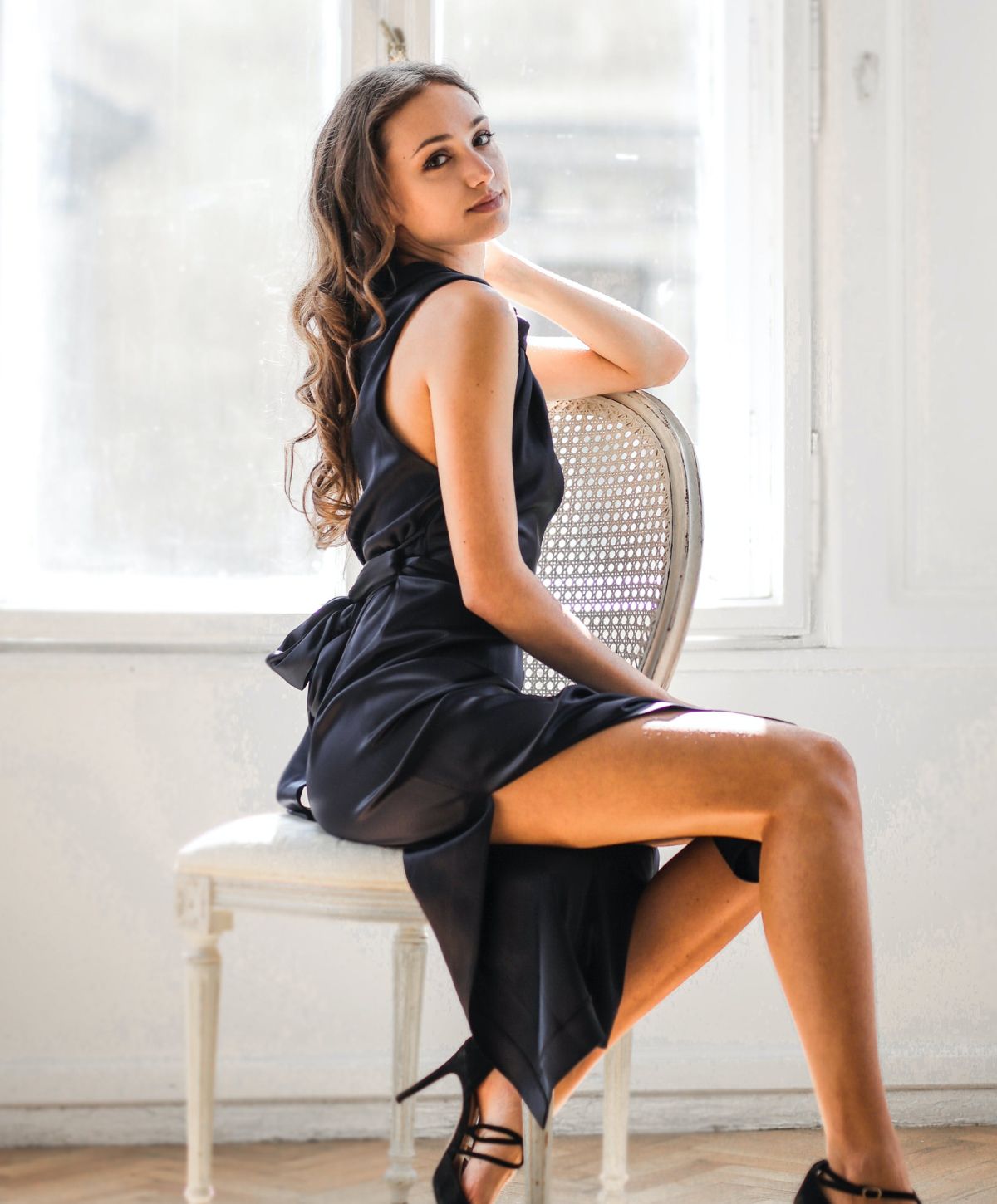 Woman in elegant black dress sitting on chair.