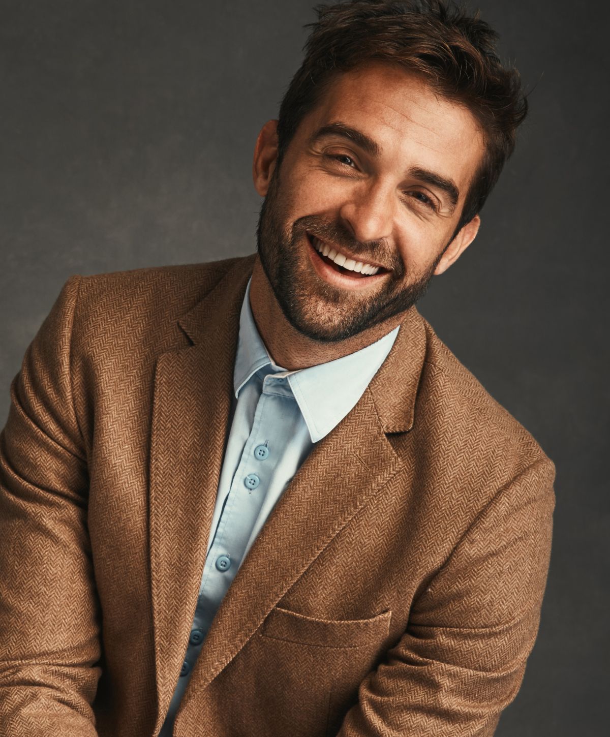 Smiling man in a brown blazer, light shirt.