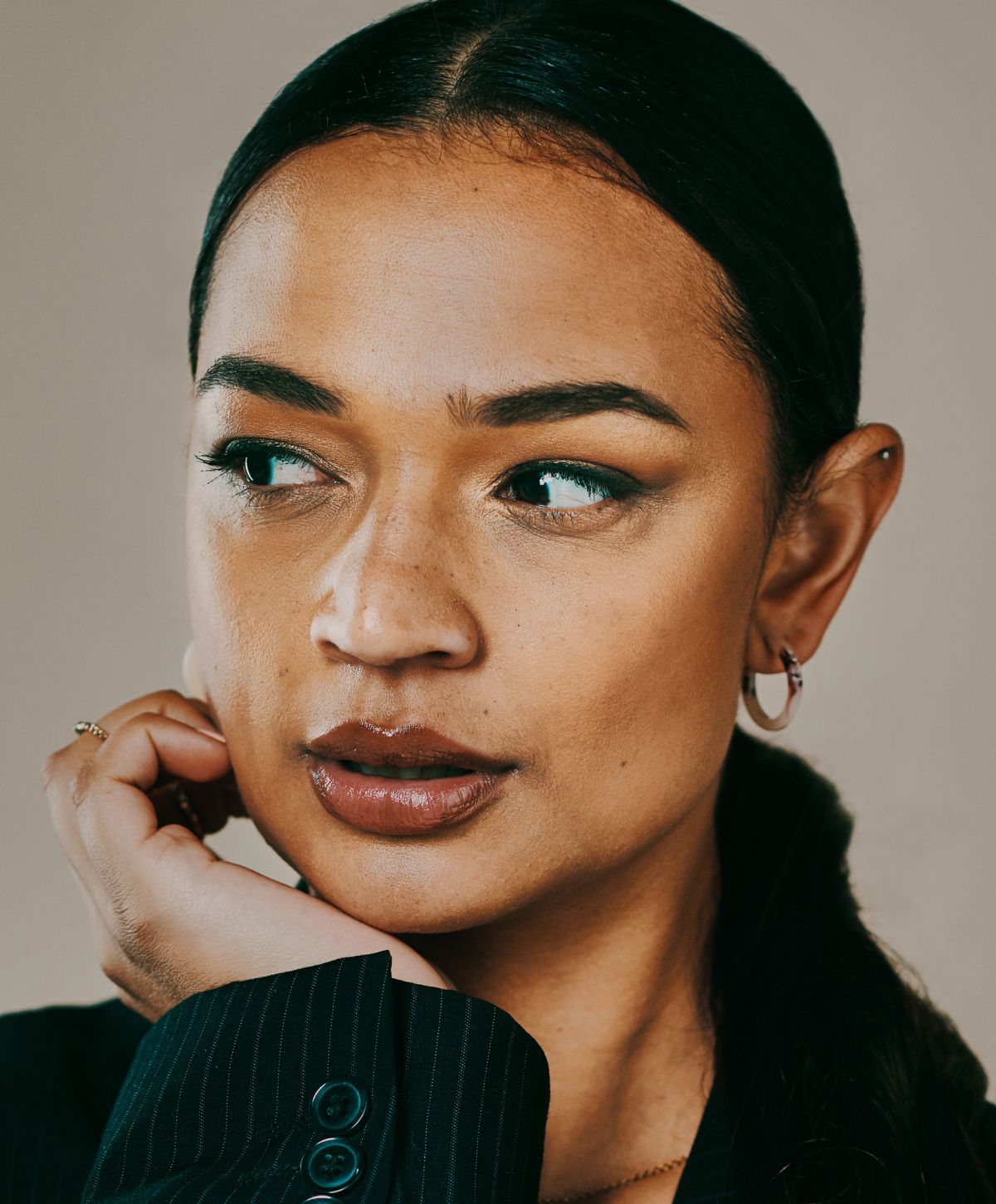Woman in blazer with hand on chin.