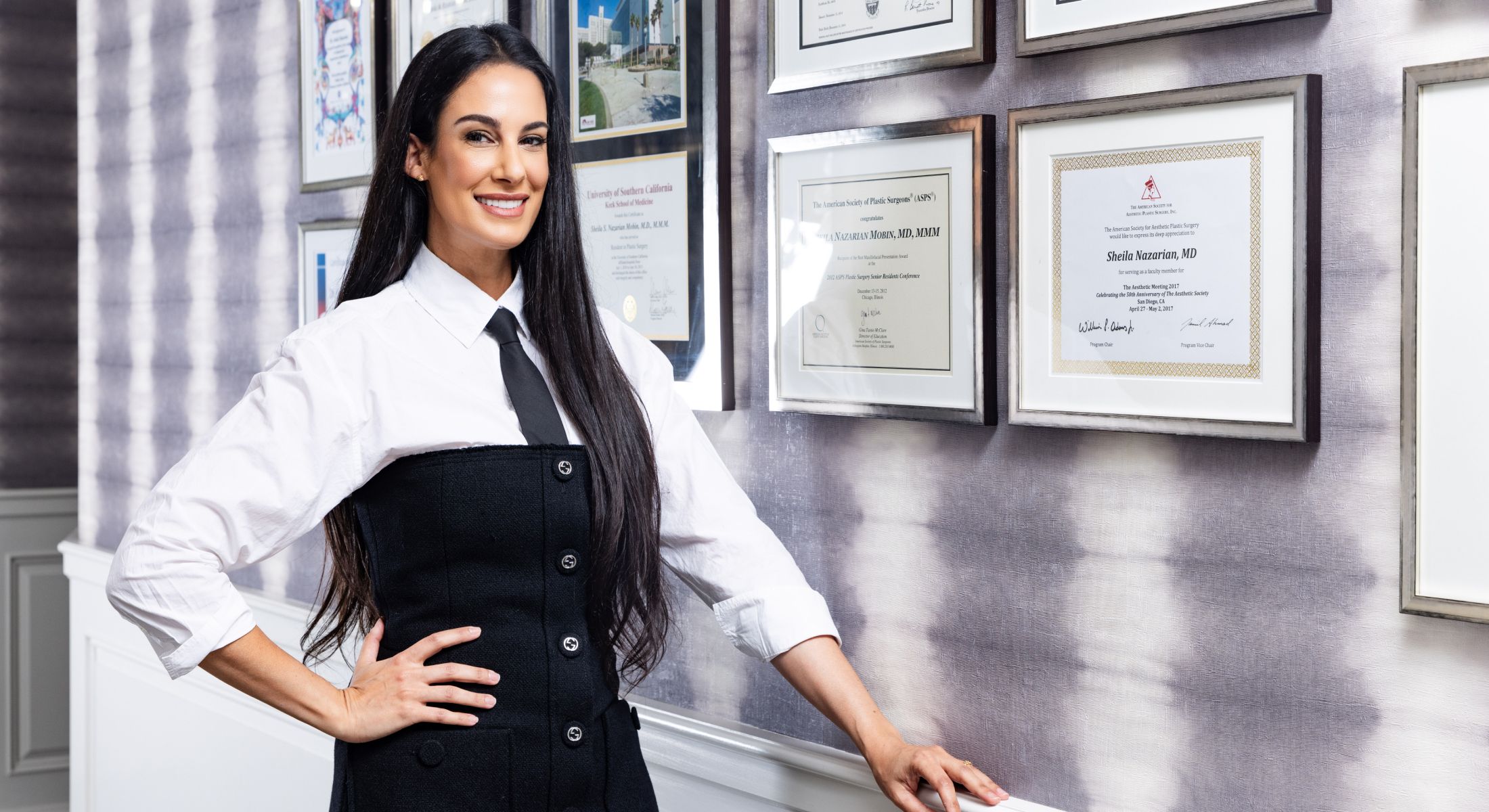 Professional woman posing next to framed certificates.