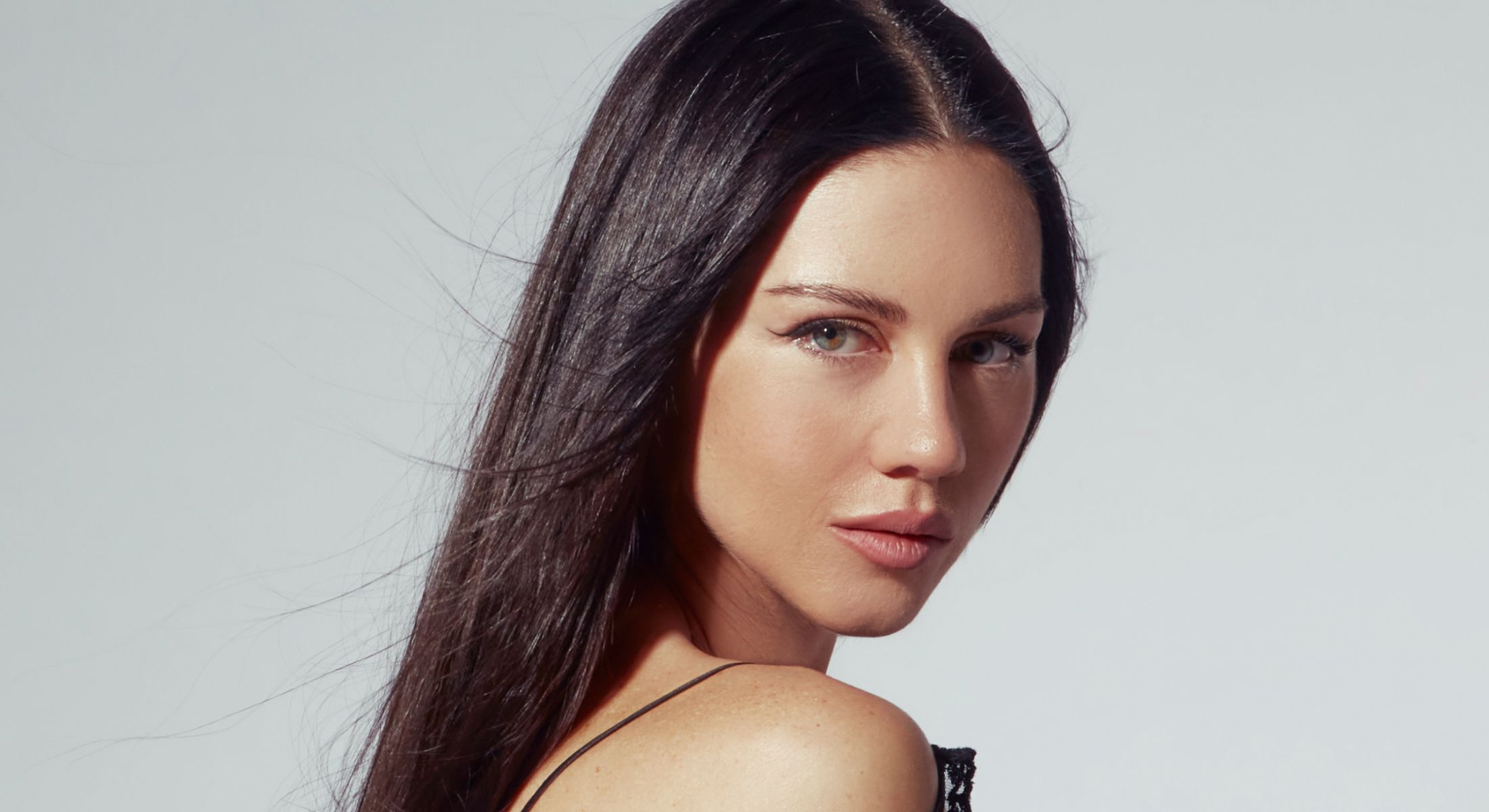 Woman with long hair, posing against gray background.