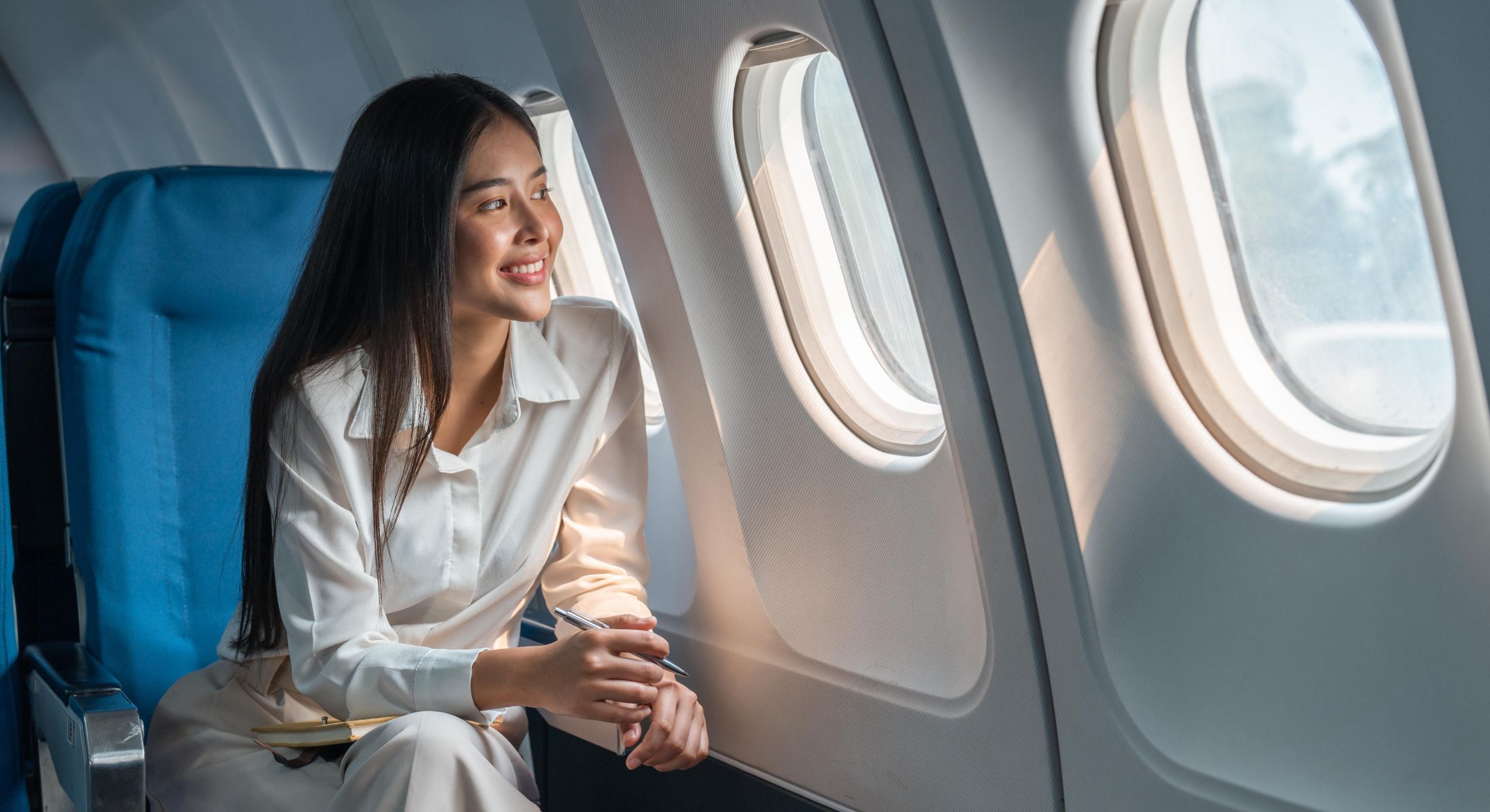 Passenger gazing out airplane window, smiling.