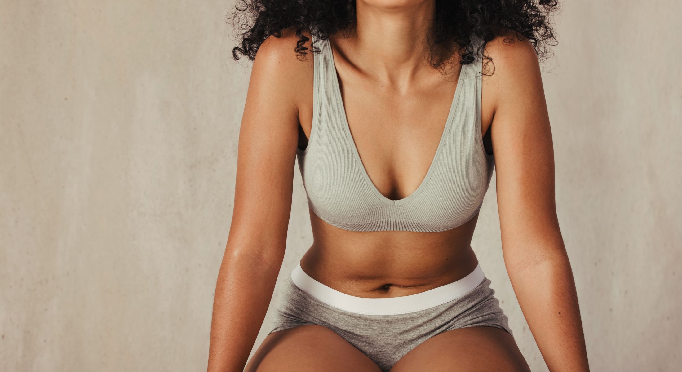 Woman in gray athletic wear against a neutral background.