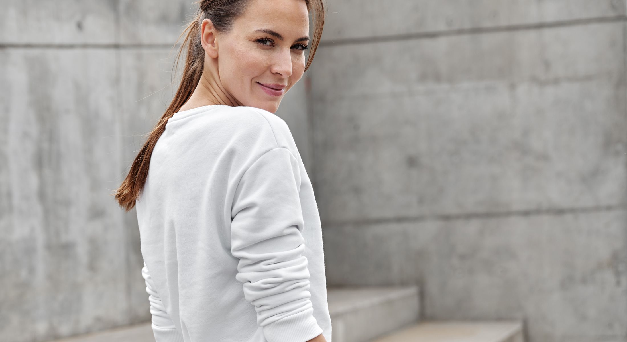 Woman smiling in casual outfit against concrete background